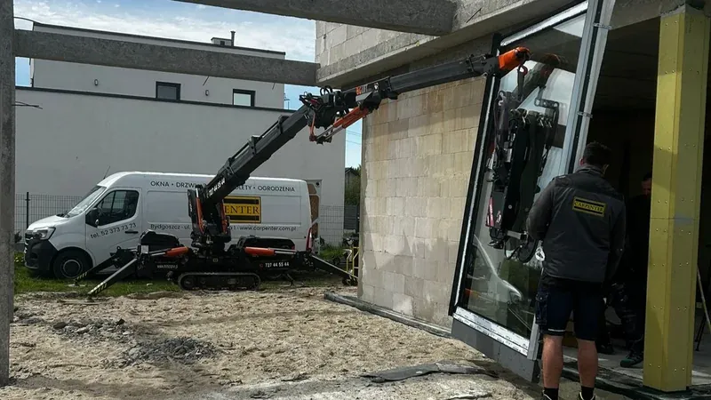 Podnoszenie dużej szyby miniżurawiem przy domu w trakcie budowy